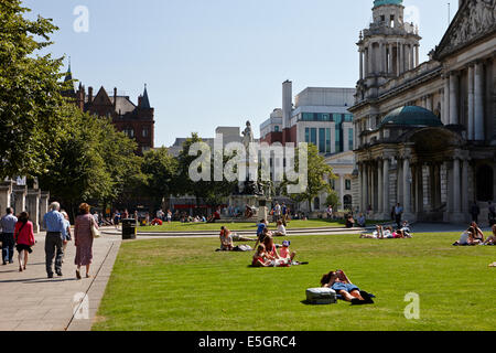 Le persone che si godono le estati calde giorno nei motivi del Belfast City Hall nel centro della città Foto Stock