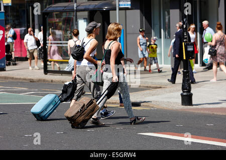 Due donne con la valigia con ruote a piedi attraverso la strada in Belfast City Centre Foto Stock