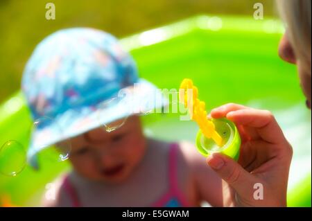Bolle di essere soffiata attraverso una bacchetta per divertire un bambino ragazza Foto Stock
