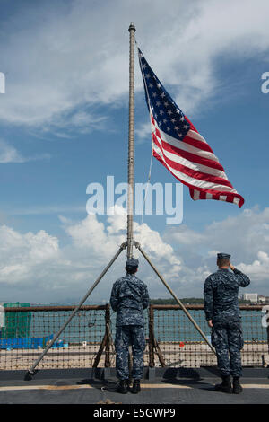 Stati Uniti Navy Cryptologic tecnico (tecnico) 2a classe Royce Penner, sinistra, solleva una bandiera americana a bordo il dock landing ship USS Foto Stock