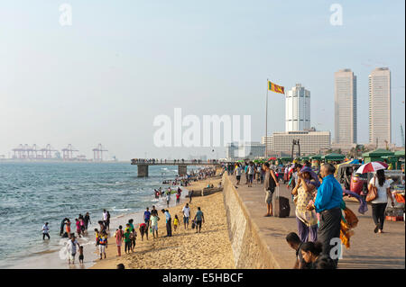 La gente a piedi lungo la passeggiata sulla spiaggia, Galle Face, grattacieli e porto dietro, Colombo, Sri Lanka Foto Stock