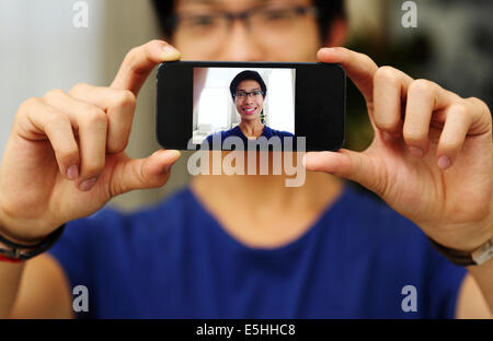 Felice uomo asiatico tenendo self foto con la fotocamera dello smartphone. Focus sullo smartphone Foto Stock