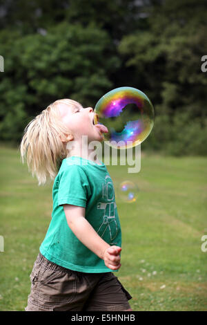Un ragazzo e ragazza di età compresa tra i 2 e i 5 chase enormi bolle intorno a un campo e pop con la loro lingua e sono aiutati a loro cattura Foto Stock
