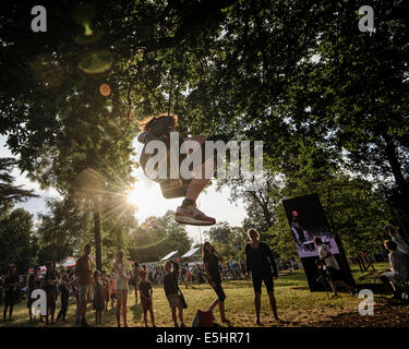 Malmesbury, Regno Unito, 25/07/2014 : Atmosfera al WOMAD - un mondo di musica, arte e danza. I bambini giocano n uno swing in alberi illuminato da una bassa sera sun. Foto di Julie Edwards Foto Stock