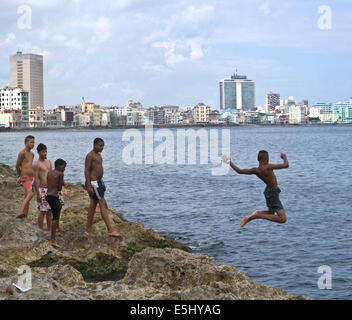 I giovani si tuffa nel mare al largo delle coste del Havana, Cuba il Malecon con lo skyline di edifici in background Foto Stock