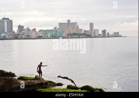 La gioventù si tuffa nel mare al largo delle coste del Havana, Cuba il Malecon con lo skyline di edifici in background Foto Stock