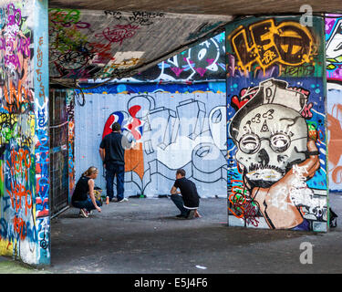 Artisti di strada al lavoro verniciatura di nuove street art e graffiti in skateboarders' undercroft sulla South Bank di Londra, Regno Unito Foto Stock