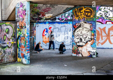 Artisti di strada al lavoro verniciatura di nuove street art e graffiti in skateboarders' undercroft sulla South Bank di Londra, Regno Unito Foto Stock