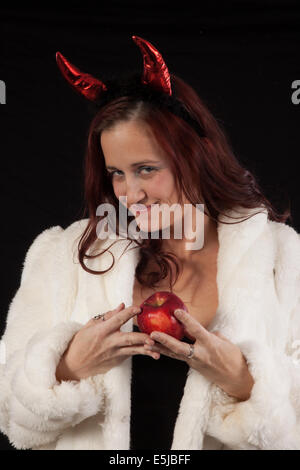 Temptress in diavolo corna e bianco pelliccia, tenendo un apple e guardando la telecamera a tentare di esso. Foto Stock