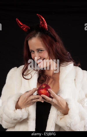 Temptress in diavolo corna e bianco pelliccia, tenendo un apple e guardando la telecamera a tentare di esso. Foto Stock