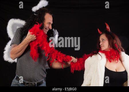 Uomo in ali d'angelo e alone bianco, con una donna in diavolo corna e red feather boa bianca e pelliccia Foto Stock