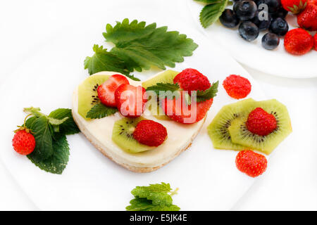 A forma di cuore e di fragola kiwi cheesecake su piastra bianca decorata con menta su piastra bianca Foto Stock