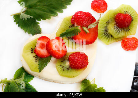 A forma di cuore e di fragola kiwi cheesecake su piastra bianca decorata con la menta Foto Stock