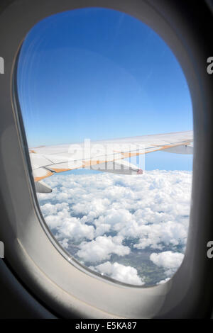 Vista passeggeri di aereo sul telaio di una finestra e un'ala di un velivolo con il bianco delle nuvole e un cielo blu battenti in Europa Foto Stock