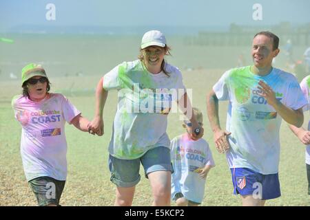 Hastings. East Sussex. Regno Unito. Il 3 agosto 2014. I partecipanti nel colore della costa della fun run lungo il lungomare della città vecchia. Guide di scorrimento lungo il 4K aveva corso a passare attraverso quattro zone di colore dove volenterosi aiutanti noto come 'Cherry Chuckers' showered corridori con un colorante colorato prima di un traguardo stravaganza di partito che coinvolga tutti gettare polvere nel cielo per creare un cloud di colore. Questo è stato un evento di beneficenza per St Michael's ospizio di St Leonards on Sea. Foto Stock