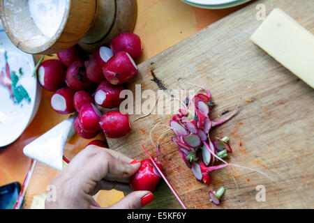 Dettaglio del tagliere e del coltello che tagliano ravanelli freschi Foto Stock