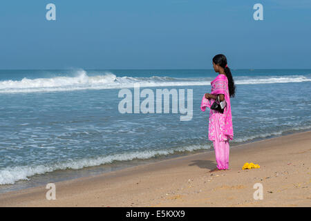 Donna che indossa un rosa shalwar kameez permanente sulla spiaggia e di fronte al mare, Varkala Kerala, India Foto Stock