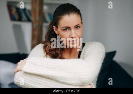 Ritratto di giovane attraente donna seduta a casa guardando la fotocamera. Abbastanza rilassato donna in ambienti chiusi. Foto Stock