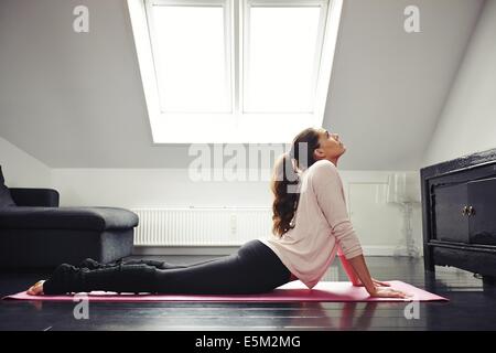 Vista laterale di un accoppiamento giovane donna fare yoga esercizio sul tappetino a casa. Femmina di stretching schiena sdraiati sul pavimento. Foto Stock