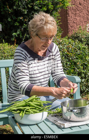 Donna anziana con artrite reumatoide in garden REGNO UNITO affettamento casa coltivati verde/i baccelli pronto per il congelamento per un uso successivo Foto Stock