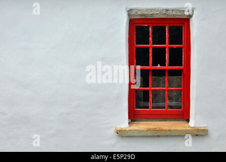 Piccolo Dipinto di rosso nella finestra a ghigliottina con pietra cill e architrave impostato in bianco-parete dipinta di un tradizionale cottage irlandese. Foto Stock