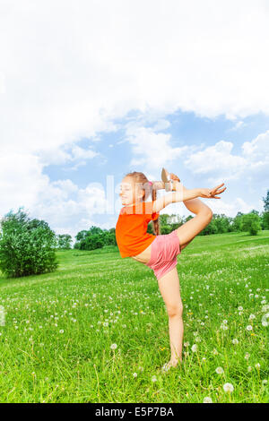 Piccola e graziosa fanciulla facendo ginnastica su un'erba Foto Stock