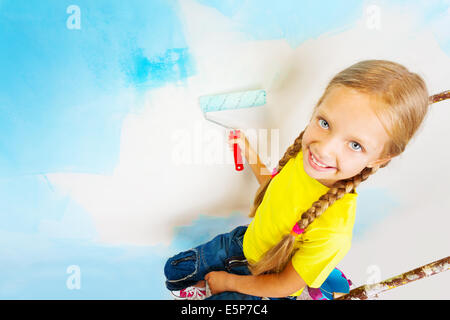 Bella bambina in giallo si siede su una scala a pioli Foto Stock