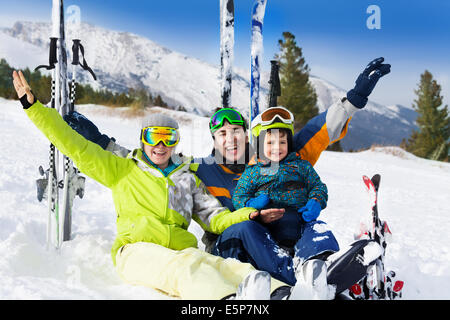 La famiglia felice con le mani fino sulla neve dopo lo sci Foto Stock