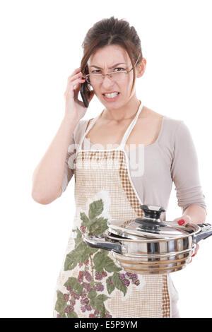 Arrabbiato donna in cucina vestito con grembiule holding pot altercating tramite telefono Foto Stock