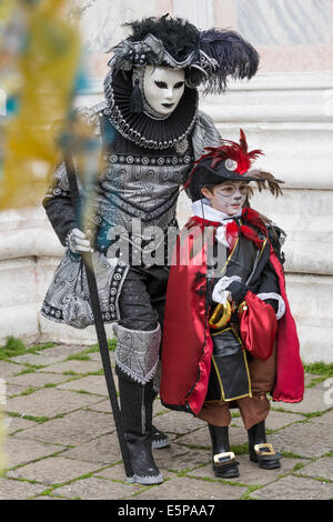 L uomo a elaborare nero e argento costume con cavalier vestito boy in cat face paint presso la chiesa di San Zaccaria, il Carnevale di Venezia. Foto Stock