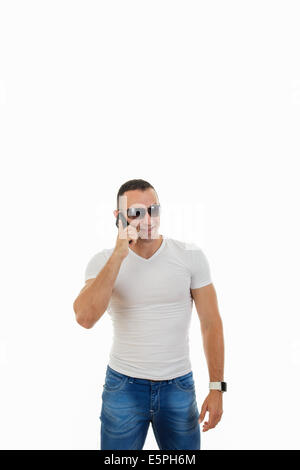 Felice uomo bello con occhiali da sole in t-shirt bianca e jeans rispondendo alle Smart Phone Foto Stock