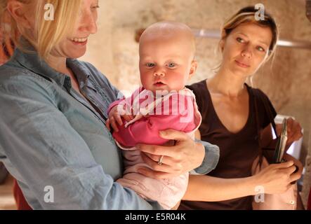 Una madre ha il suo mese 8 bambino a un operatore sanitario professionale che si prenderà cura di lui durante la sua giornata lavorativa. Foto Stock