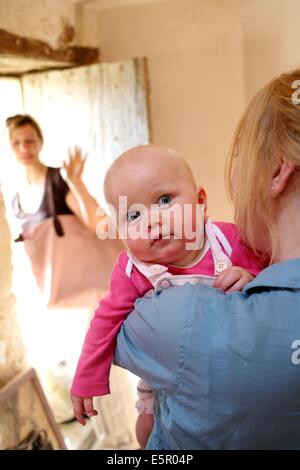 Una madre ha il suo mese 8 bambino a un operatore sanitario professionale che si prenderà cura di lui durante la sua giornata lavorativa. Foto Stock