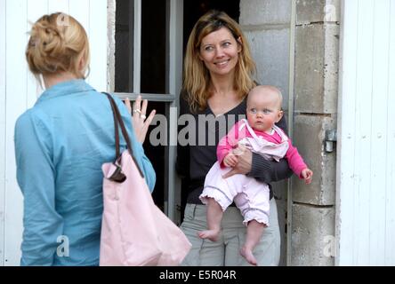Una madre ha il suo mese 8 bambino a un operatore sanitario professionale che si prenderà cura di lui durante la sua giornata lavorativa. Foto Stock