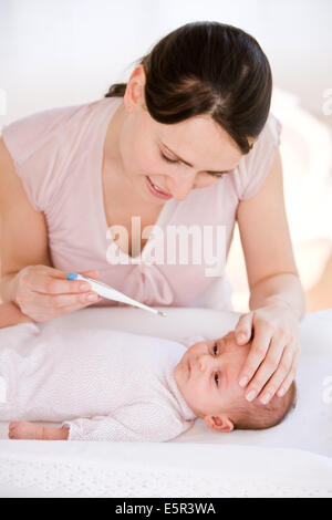 Madre controllando la temperatura dei suoi 2 mesi baby febbrile con un termometro digitale. Foto Stock