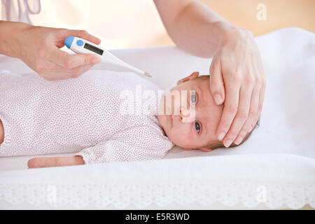 Madre controllando la temperatura dei suoi 2 mesi baby febbrile con un termometro digitale. Foto Stock