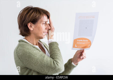 Senior donna guardando una Griglia di Amsler per rilevare la degenerazione maculare. Foto Stock