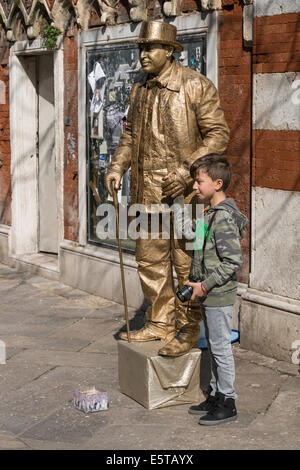 Giovane ragazzo sta con golden living statua street performer durante il carnevale di Venezia. Foto Stock