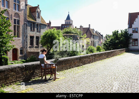 Donna che utilizza computer portatile seduti sulle strade del centro della città di Bruges, Belgio Foto Stock
