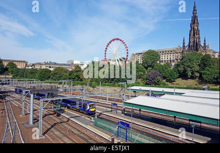 Un turbostar Scotrail treno arriva alla stazione di Waverley di Edimburgo in Scozia con la grande ruota panoramica Ferris e Monumento Scott dietro Foto Stock