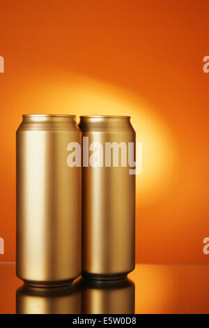 Due golden lattine di birra su sfondo arancione Foto Stock