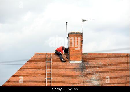 Un operaio salendo una scala per riparare la parte superiore di un tetto England Regno Unito Foto Stock