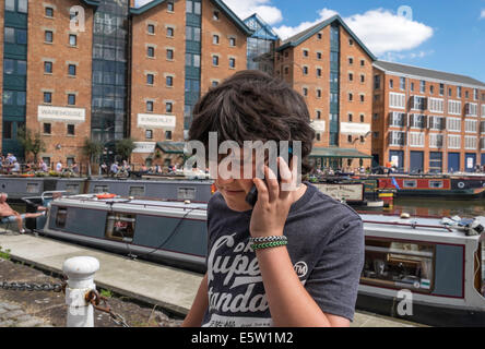 Ragazzo giovane SUL CELLULARE IN GLOUCESTER DOCKS davanti a vecchi magazzini e imbarcazioni strette GLOUCESTER England Regno Unito Foto Stock