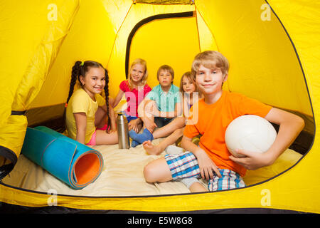 Ragazzo con palla e amici in tenda da campeggio Foto Stock