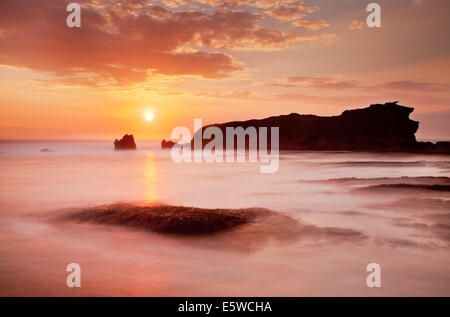 Tramonto sul mare di pile. bellissimo cielo arancione con golden sun quasi orizzonte su misty mare con stack stagliano rock. lunga esposizione tecnica fotografica Foto Stock