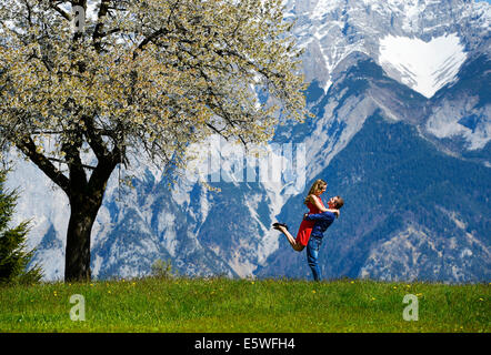 Gli amanti abbracciando accanto a un albero di fioritura in primavera, montagne sul retro, Tirolo, Austria Foto Stock