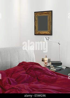 Dettaglio del letto con coperta di rosso in una moderna camera da letto con lampada da tavolo Foto Stock