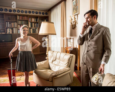 Giovane coppia vintage in salotto con telefono vintage e aspirapolvere Foto Stock