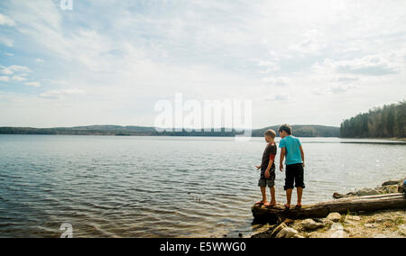 Due ragazzi in piedi su albero caduto guardando in giù nel lago Foto Stock