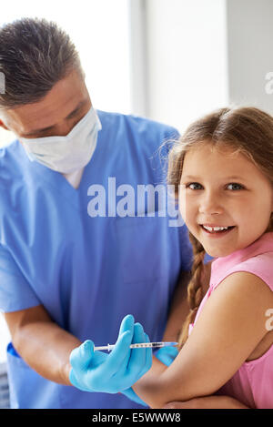 Ragazza sorridente guardando la fotocamera mentre medico fanno di lei una iniezione nelle cliniche Foto Stock